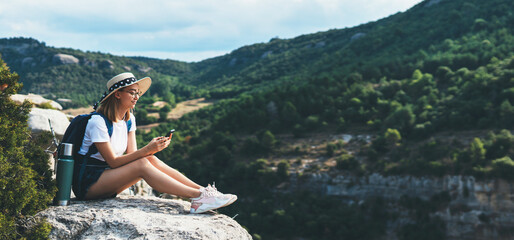 girl traveler in hat resting during vacation in nature and plans route online map in smartphone,...