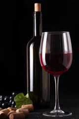 Wine bottle and glass of red wine on dark textured surface