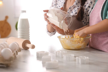 Mother and daughter making dough at table in kitchen, closeup