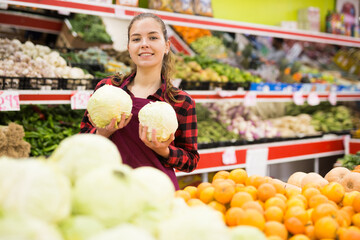Portrait of a smiling girl of the seller near the counter, holding a cabbage in her hands