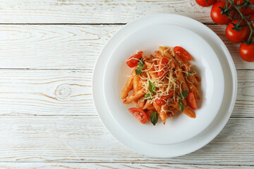 Plate with pasta with tomato sauce, and tomatoes on white wooden table