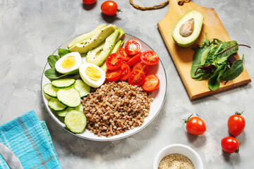 Vegan lunch bowl with avocado, egg, cucumber, tomato and buckwheat on concrete background