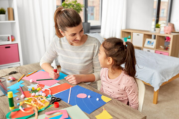 family, art and craft concept - mother spending time with her little daughter with glue making applique of color paper at home