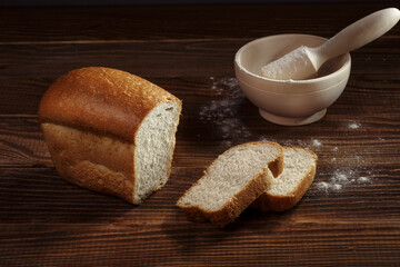 Sliced wheat bread with flour on a wooden background
