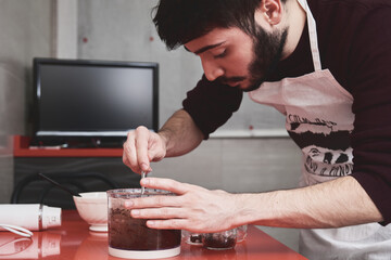 Young caucasian man in apron cooking in a kitchen. He is preparing a sweet with chocolate.