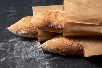 food, baking and cooking concept - close up of baguette bread in paper bags on table over dark...