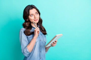 Photo of minded happy young woman look empty space hold notebook good mood isolated on teal color...