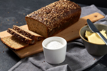 food, baking and cooking concept - close up of bread, butter in bowl, table knife and salt in cup on towel