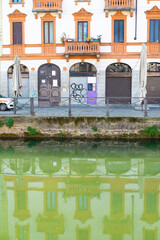 Facade of an old building in Navigli neighborhood, in Milan, Italy. The reflection of the building is visible on the water.