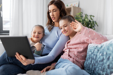 Fototapeta premium people, family and technology concept - happy mother and two daughters with tablet pc computer having video call at home
