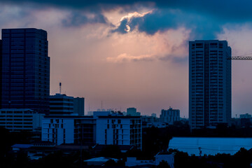 The backlit shot of the tall buildings stand out among small buildings and houses, which has a background of clouds blocking the moon and sky.
