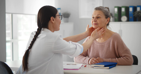 Professional physician checking neck lymph nodes of old woman