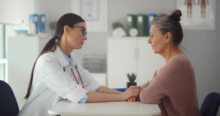 Female doctor supporting crying senior woman after hearing diagnosis in clinic