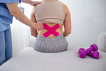 Chiropractor applying two kinesiology tapes to the back of a woman for pain relieve. Patient...
