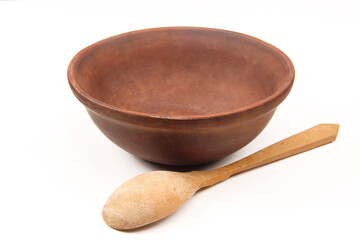 Rustic old traditional kitchen utensils in the form of a clay plate or bowl on a white background. Empty antique dishes. The spoon is placed next to the ceramic bowl.