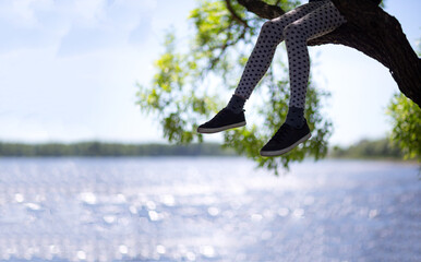 girl sits on a tree, only legs are visible on the background of the river