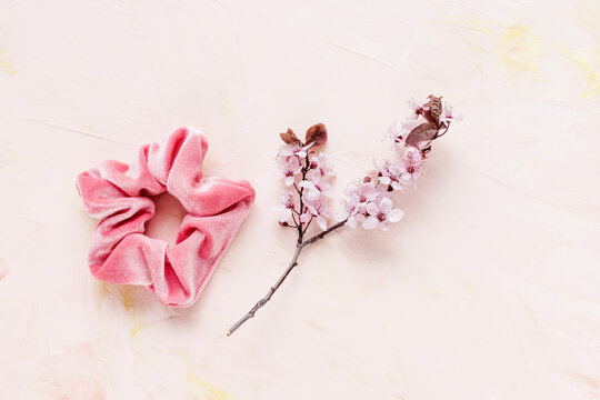 One trendy velvet scrunchie and fresh spring branch with pink flowers on pastel backround. Flat lay, top view. Diy accessories, hairstyle, lifestyle, spring and summer outfit ideas concept, copy space