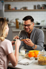 Happy man enjoying in breakfast with his girlfriend. Loving young couple drinking coffee and eating sandwich at home..