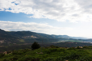 Obraz premium A view of a mountain range and a green valley in the morning at sunrise, against a dramatic backdrop of blue skies and clouds. North District Israel. High quality photo. Travel concept hiking