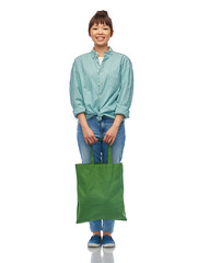 sustainability and people concept - happy smiling young asian woman in turquoise shirt and jeans with green reusable canvas bag for food shopping over white background