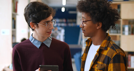 Diverse students working together in modern school library and using digital tablet