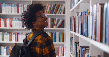 Back view of young happy african student looking around in modern library