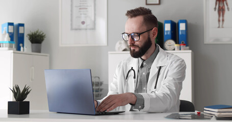 Young male doctor working on laptop in clinic office