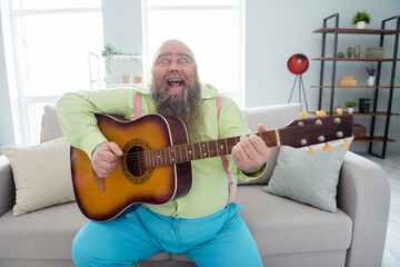 Photo of pretty impressed big abdomen guy dressed green shirt singing songs playing guitar indoors apartment room