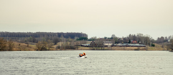 A family enjoying its weekend motor boat ride. Father and his sons in orange life suits against the rural landscape and grey clouds.