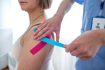 Young woman wearing blue and pink kinesio therapy tape on her shoulder. Alternative medicine rehab....