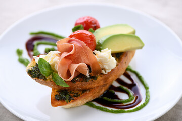 Toasted baguette toast with pesto sauce, a slice of Parma ham, mozzarella, tomato and avocado