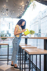 Woman in casual clothes watering plant in cafe