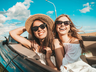 Portrait of two young beautiful and smiling hipster female in convertible car. Sexy carefree women...