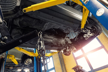 Bottom POV big modern SUV car with removed gearbox raised on lift elevator at workshop service maintenance station center. Vehicle check-up and repair. Underbody chassis and suspension parts - obrazy, fototapety, plakaty