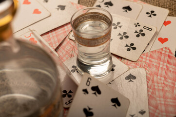 Playing cards, a glass of vodka and a decanter of vodka on a table covered with coarse burlap.