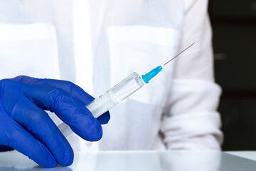 Doctor in white gown and medical syringe, hospital background, blue gloves, needle close-up