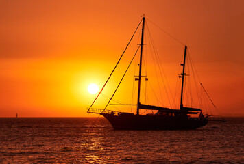 Fototapeta na wymiar Close view of silhouette of sailing boat with sails down against sun at sunset, sun glare on sea waters. Romantic seascape