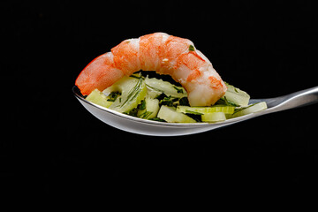 Shrimps with salad in a spoon on a black background