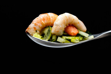 Shrimps with salad in a spoon on a black background