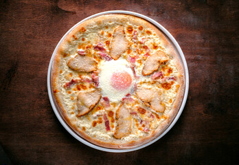 Homemade Carbonara pizza with bacon and chicken breast, egg and cheese on a wooden background. Unconventional pizza recipes
