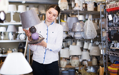 Young woman is buying new lamp on table in furniture store