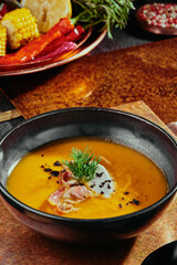 Pumpkin cream soup with bacon in a black plate on a metal background.
