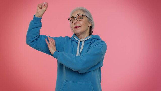 I am strong and independent. Senior old granny woman showing biceps, looking confident, feeling power strength to fight for rights, energy to gain success win. Elderly grandmother on pink background