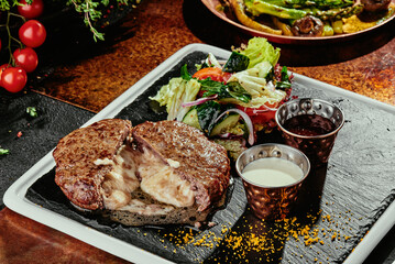meat chop with cheese inside and grilled vegetables on a black plate. copper background