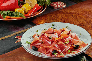 cold smoked meat plate with jamon, with olives and soybean sprouts on a white plate and grilled vegetables on a copper background. 