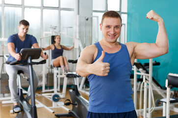 Fototapeta na wymiar Portrait of cheerful sporty man posing at gym with his friends on background