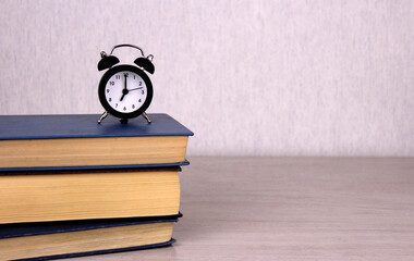 Small black clock on a stack of books on a wooden table