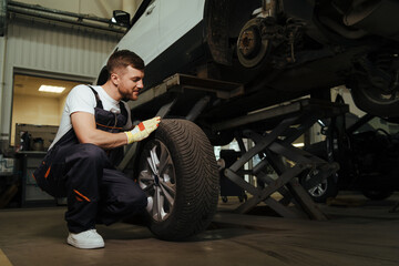 Fototapeta na wymiar Mechanic changing a wheel and tire of modern car in workshop