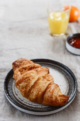 Breakfast with croissant, jam, juice and tangerine on greige linen tablecloth. Selective focus