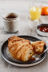 Breakfast with croissant, jam and hot chocolate, juice and tangerine on greige linen tablecloth. Selective focus